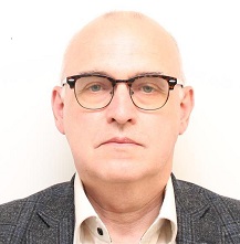 Profilbild på Åke Karlsson. Åke bär glasögon, vit skjorta och grå kavaj.
