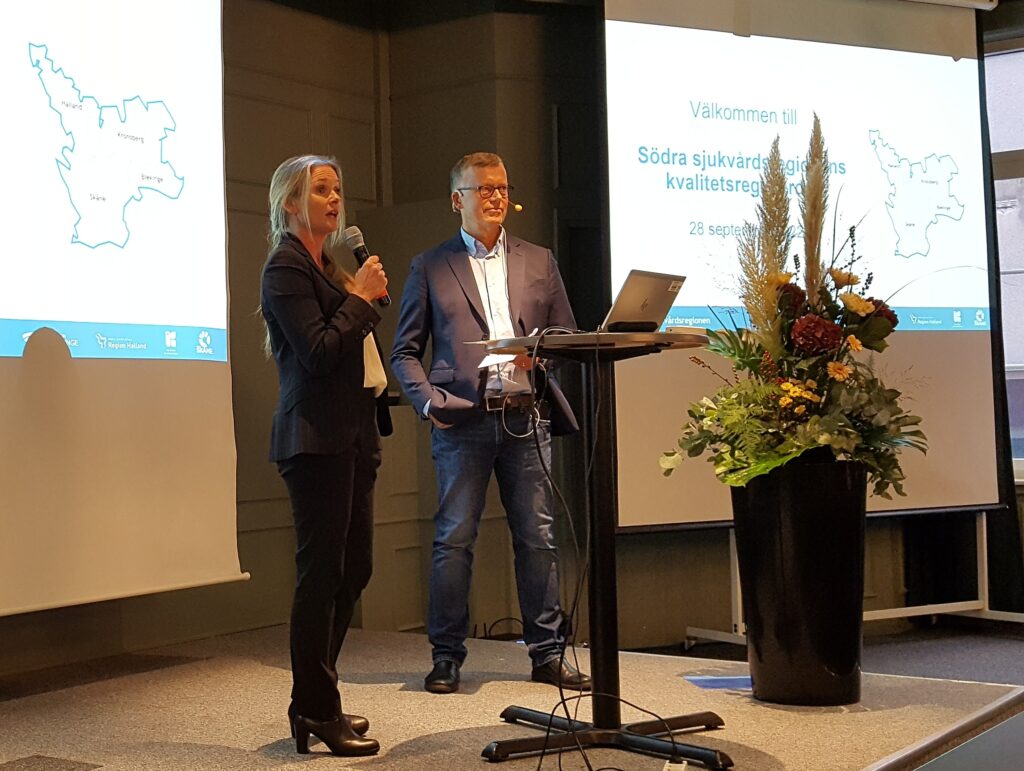 Maria Rejmyr Davis och Sven Oredsson står på en scen och inledningstalar i mikrofon med åhörare på Södra sjukvårdsregionens registerdag.