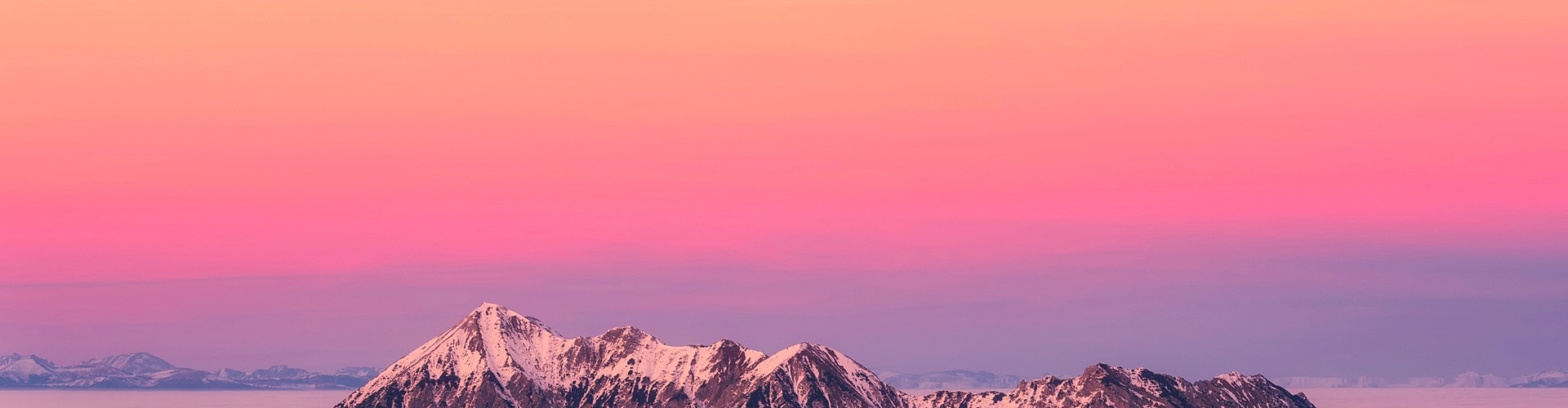 Himmel i skiftande orange, rosa och lila färg. I förgrunden syns snötäckta bergstoppar.