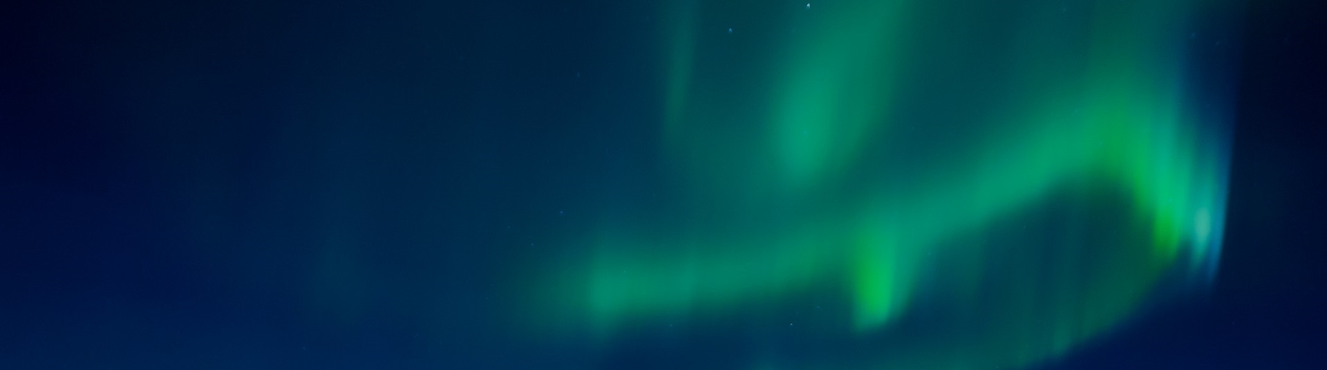 Grönt norrsken mot mörkblå natthimmel.